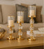 Three gold candle holders with candles on a table in a living room setting.