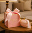 Pink gift box with a bow and a matching pink candle on a wooden table.