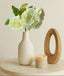 White vase with white rose bunch on a beige surface with a candle and wooden object.