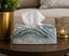 Marble-patterned tissue box on a table with a candle and plant in the background