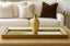Gold vase on a gold finished mirror tray with a beige sofa and decorative pillows in the background