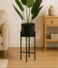Black plant stand with a potted plant in a living room setting.
