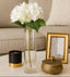 Decorative setup with a vase of white flowers, black candle, gold box, and picture frame on a table.