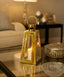 Gold lantern with a candle on a reflective surface in a softly lit room.