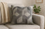Geometric grey patterned pillow on a beige sofa with a plant in the background