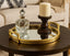 Decorative glass vase and candle on a round wooden table with a mirror metal tray.
