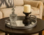 Decorative silver mirror tray with a candle and glass container on a table in a living room setting.