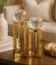 Two gold decorative stands with clear glass spheres on a wooden surface.