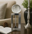 Decorative silver stand with clear globe on a table with a book and plant in the background