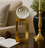 Decorative glass sphere on a gold stand with a book and plant in the background