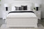 Hamptons white bed frame styled with black lamps, cushions and matching bedside tables in a bright room.