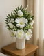 Bouquet of white flowers in a vase on a wooden table against a neutral wall.