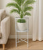 White metal plant stand with a green plant next to a beige sofa in a room.