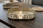 Decorative gold mirror tray on a wooden surface with books and a woven basket in the background.