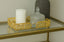 Decorative gold rectangle tray with a candle and glass container on a reflective surface.
