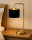 Gold table lamp with a black shade on a wooden nightstand.