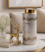 Decorative cylindrical vase with gold accents on a marble table in a living room setting.