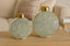 Two decorative vases with gold lids on a wooden surface, with a blurred background.