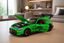 A bright green Mercedes-Benz AMG GT Pro scale model car with its hood open, displayed on a light wood table in a modern, softly blurred living room setting.