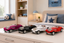 Four miniature vintage convertible toy cars in pink, black, white, and red are lined up on a light-colored dresser in a styled bedroom setting.