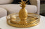 Gold pineapple decorative item on a matching gold round tray set on a table.