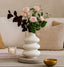 White vase with pink flowers on a table with a neutral background