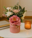 Pink vase with flowers on a table next to a candle