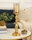 Gold candle holder with a lit candle on a table in a cozy living room setting.