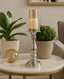 Silver candle holder with a candle on a marble table, surrounded by potted plants.