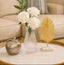 Decorative items including a ribbed vase with white flowers, a gold leaf sculpture, and a silver apple on a table.