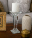 Decorative glass candle holder with a white candle on a wooden surface.