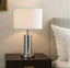 Silver Table lamp with white shade on a nightstand next to a bed