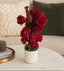 Red floral arrangement in a white pot on a table with a neutral background