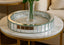 Round mirrored coffee table with decorative base in a living room setting