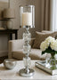 Decorative candle holder on a table with a candle, surrounded by a vase of flowers and other decor items in a living room setting.