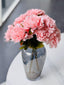 Two soft pink artificial bloomed peony bunches styled in a smoked glass vase on a marble table.