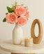 Soft pink artificial bloomed peony bunch styled in a white ribbed vase on a round table with a candle.