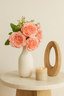 Coral artificial rose bunch, 31cm, styled in a white ribbed vase on a round table with a candle.
