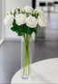 Six white artificial rose stems in a clear glass vase on a white surface.