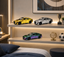 Three metallic toy model sedans in gold, silver, and iridescent green-purple colors displayed on white shelves in a modern bedroom setting.