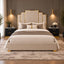 A luxury upholstered bed centered in a modern bedroom, featuring a tall geometric headboard with gold trim, cream bedding, neutral pillows, matching nightstands, and warm pendant lighting.