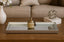 Decorative mirror silver tray on a wooden coffee table with a vase, books, and decorative ball.