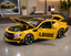 A bright yellow scale model of a sports car with its hood and trunk open, displayed on a polished gray tabletop in a modern room setting. The side of the car features the text 'LBWK' in black.
