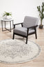 Round silver rug styled in a modern living room with a grey chair, table, and indoor plants.