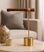 Gold lamp on a table with a vase and small cup in a room setting