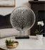 Decorative silver round piece with black tree design on a white surface