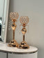 Stylish gold crystal ball candle holders displayed on a tabletop with lush green background — featuring shimmering crystals and a hammered gold base for an elegant decorative touch.