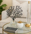Decorative black tree sculpture on a glass coffee table with a gold lamp and a book.