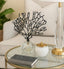 Decorative black tree sculpture on a glass coffee table with a gold lamp and a book.