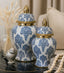 Decorative blue and white jars with gold lids on a table.